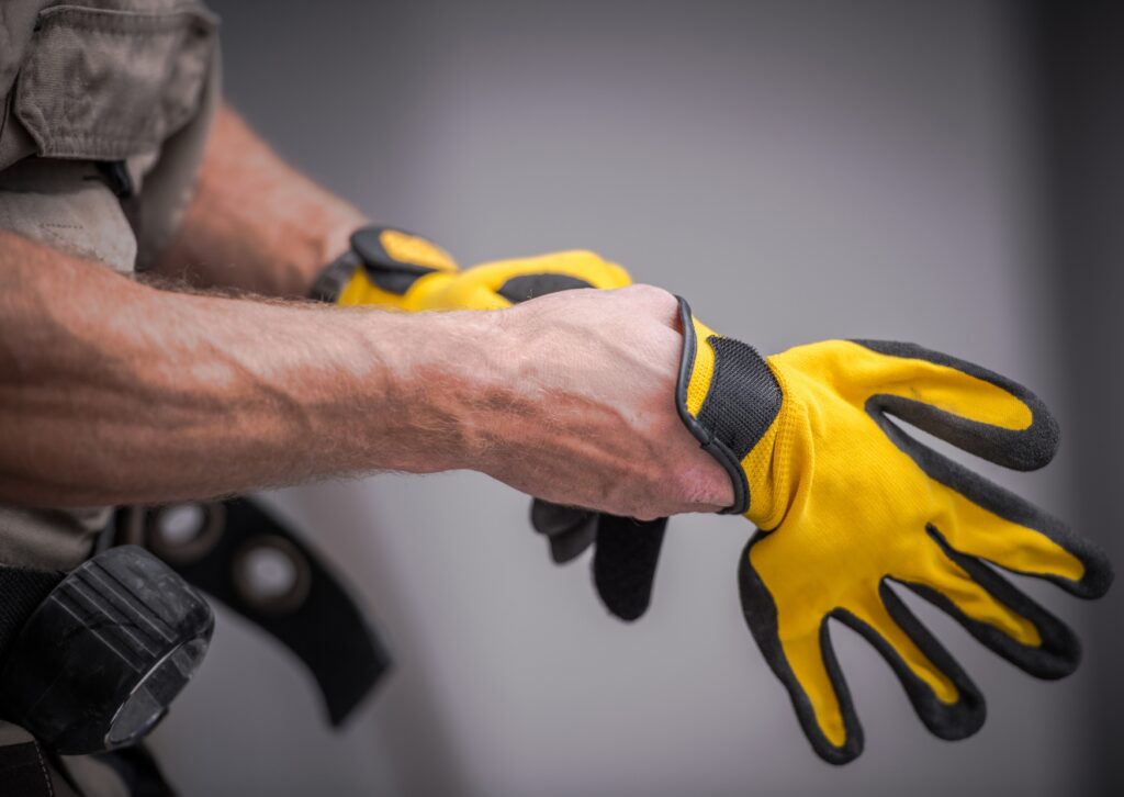 A worker puts on yellow and black protective gloves, preparing for pressure washing. The close-up image shows his forearms and part of his work belt.