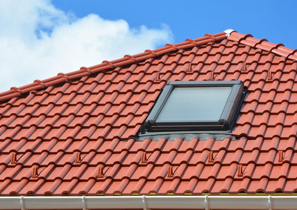 A close-up view of a red roof with a clean skylight under a blue sky with white clouds, showcasing the results of effective canopy tile cleaning.