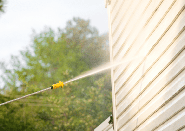 Soft washing a home exterior, using a low-pressure system to gently clean siding and enhance curb appeal.