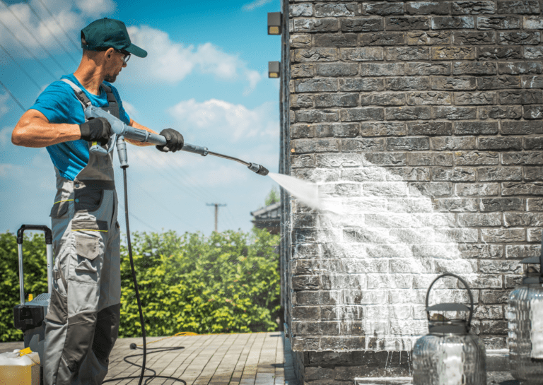Workers demonstrate the soft washing benefits by cleaning a brick wall, highlighting its efficiency and care for surfaces.