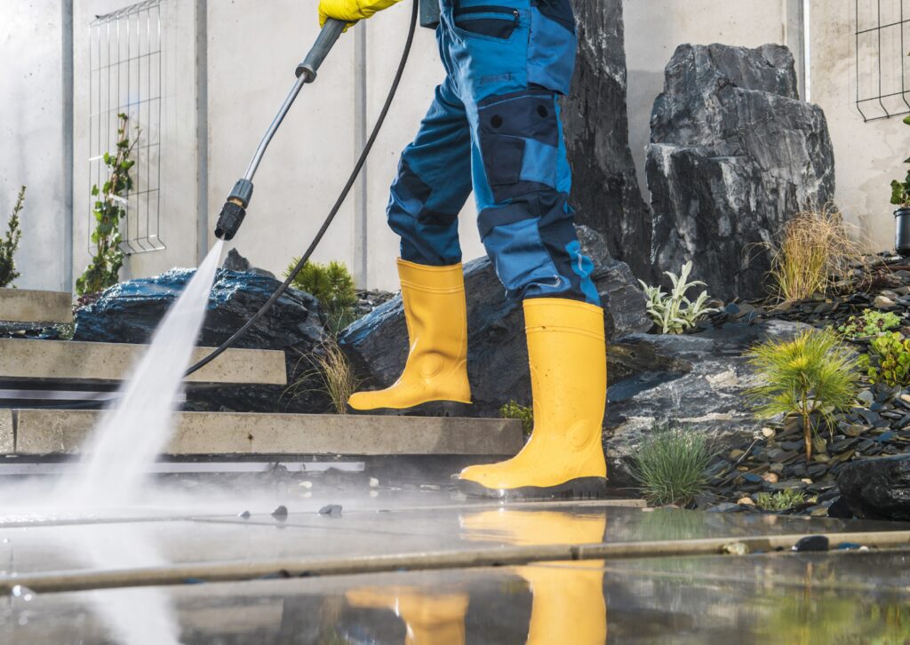 Worker using a pressure washer on outdoor tiles, showcasing the difference between soft washing and pressure washing.