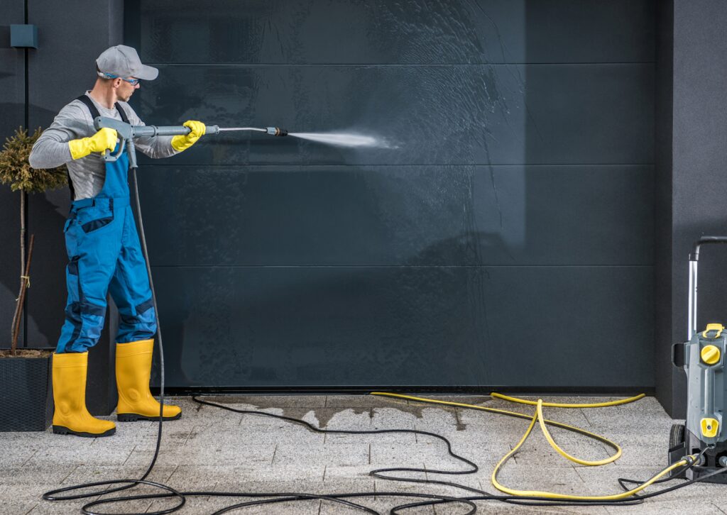 Worker using a pressure washer on a garage door, showing exterior soft washing benefits on surfaces.