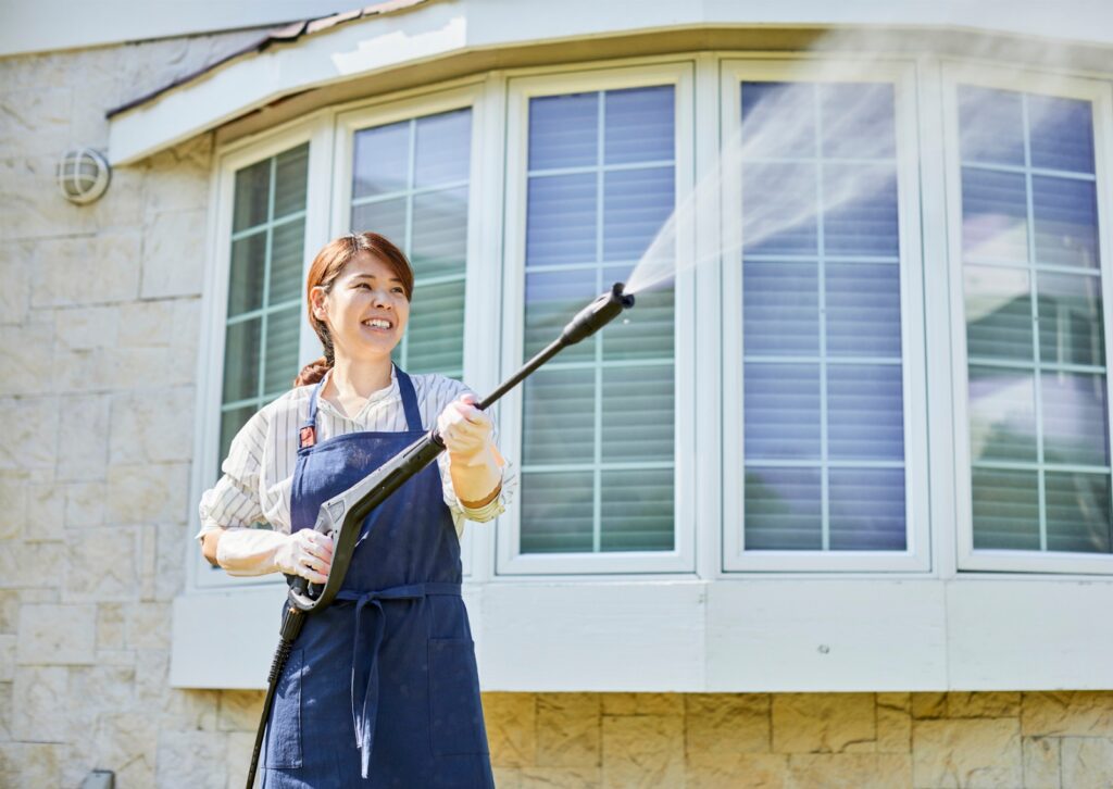Woman pressure washing home exterior with a smile, visually answering what is the process of softwashing.