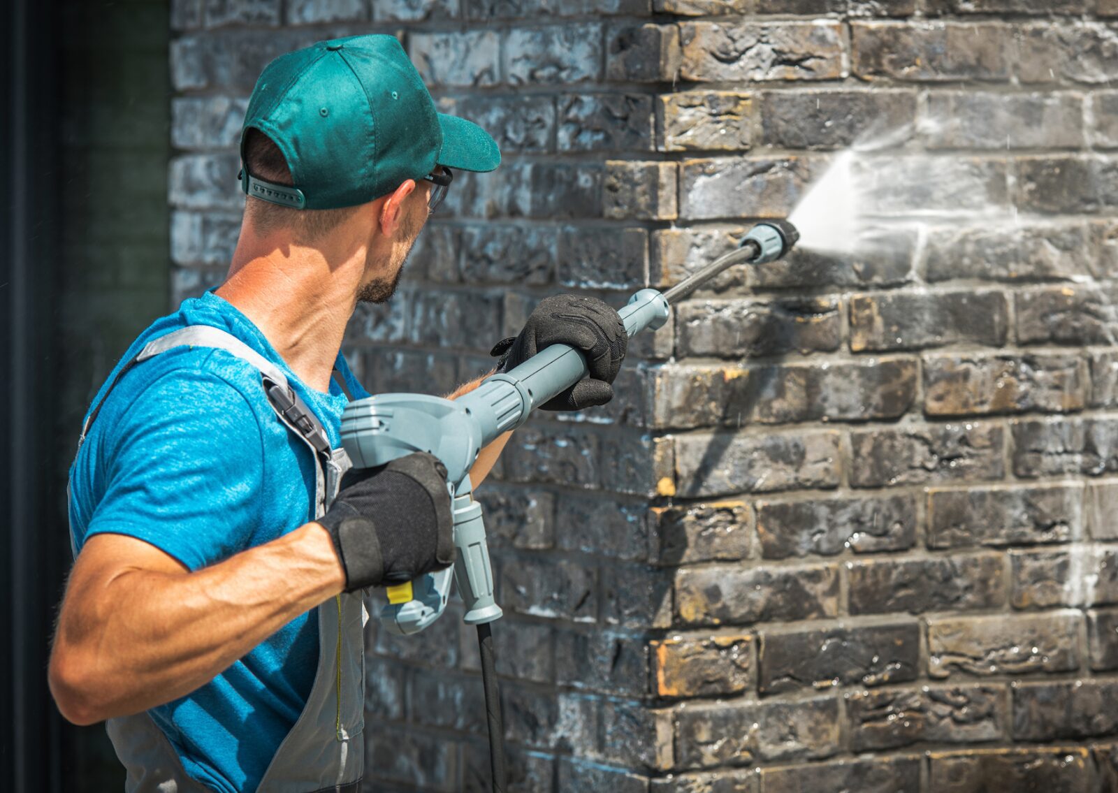 Man using pressure washer on brick wall, illustrating example of what does soft washing a house mean.