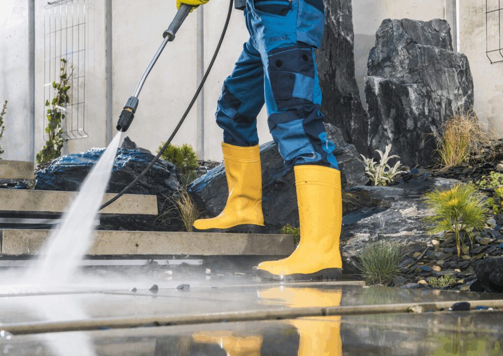 Technician in yellow boots pressure washing concrete to highlight the benefits of soft washing your house.